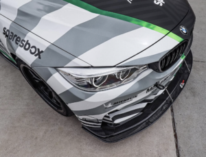 Close-up of a BMW M4 race car with a custom car wrap featuring Sparesbox and Michelin branding, aggressive front splitter, and racing modifications.